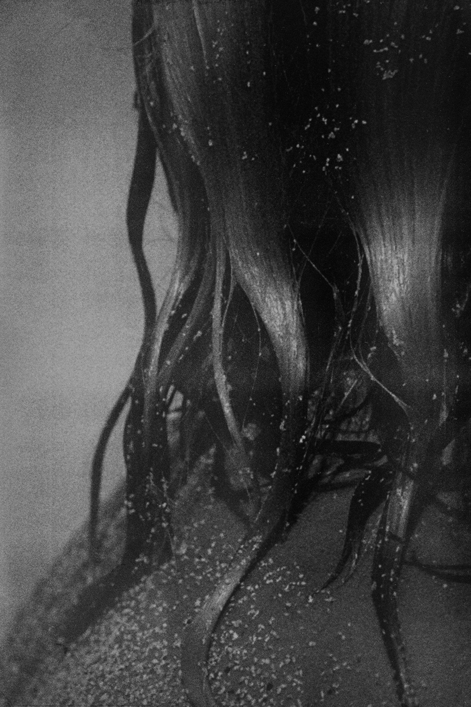 Wet hair falling over a shoulder, flecked with sand, in black and white